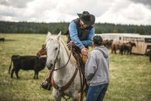 Ranch Broker Bill Boyce on horseback shaking hands with a man